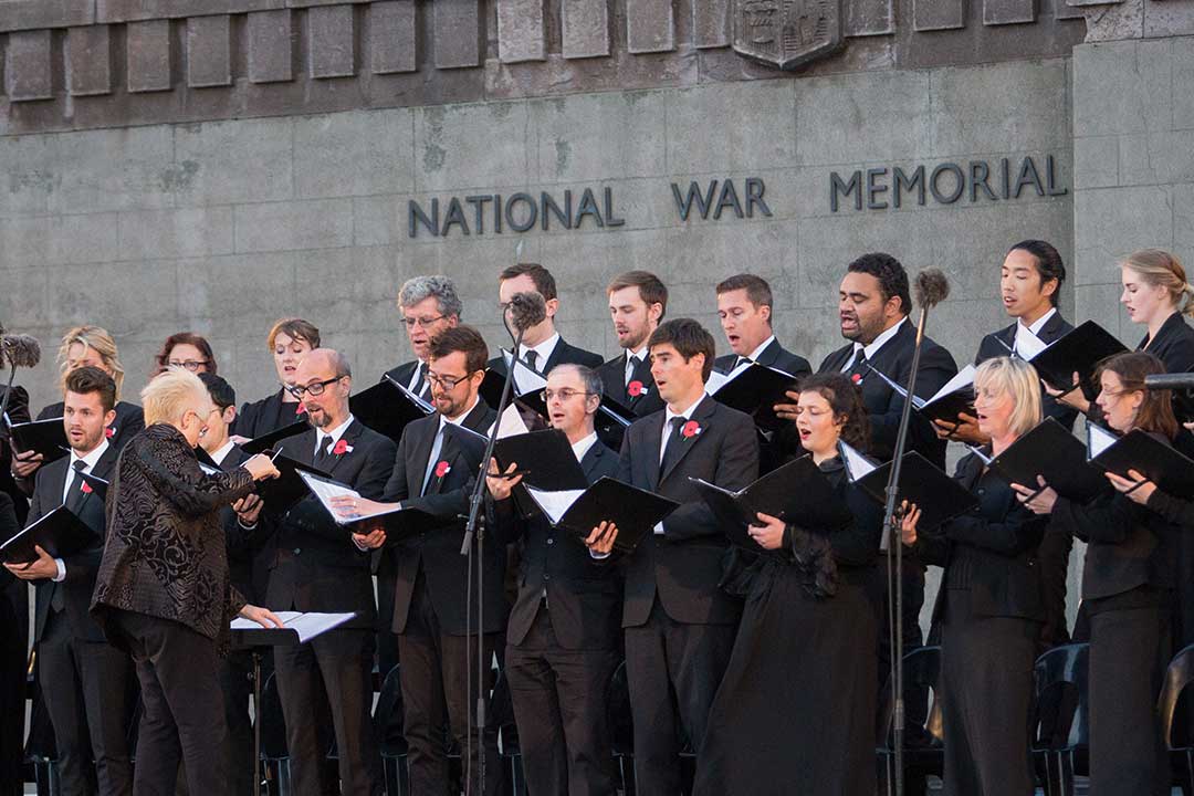 A choir wearing all black singing in front of the National War Memorial