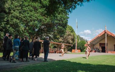 Group of people walking onto a marae. They are being met by two people performing a wero